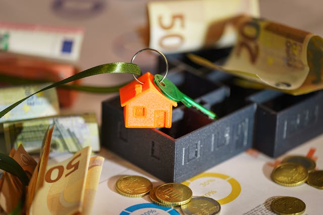 a small model house with a key attached surrounded by cash
